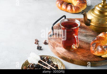 Türkischer schwarzer Tee. Eine Glasschale türkischer schwarzer Tee und knuspriger türkischer traditioneller Bagel auf grauem Betontischhintergrund. Frühstücksgebäck-Konzept. Traditionelles türkisches Heißgetränk. Stockfoto