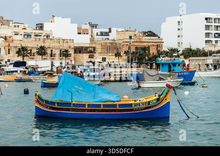 Marsaxlokk, Malta - 13. April 2025: Traditionelle, farbenfrohe maltesische Fischerboote namens Luzzu mit hellblauen, gelben und roten Details, die im malerischen Hafen von Marsaxlokk ankern Stockfoto