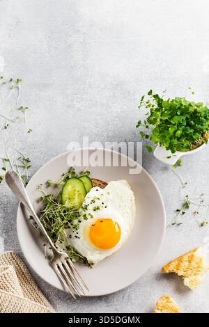 Traditionelles englisches Frühstück mit Spiegeleiern mit Rucola microgreen in grauer Keramikplatte auf grauem Beton altem Hintergrund. Draufsicht. Stockfoto