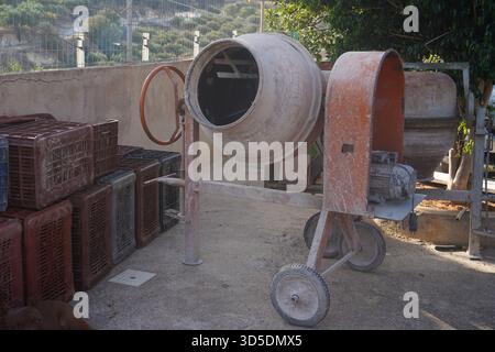Ein alter, verwitterter Zementmischer steht an einem sonnigen Tag im Freien, bereit für den Einsatz auf einer Baustelle. Stockfoto