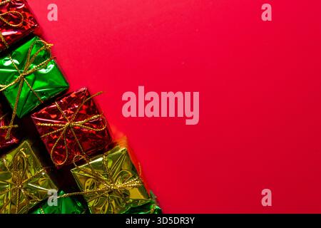 Eine glänzend grüne, rote und goldene Geschenkschachtel mit goldenen Fäden sitzt vor einem roten Hintergrund. Weihnachten, Feiertage oder Verkaufsereignisse. Stockfoto