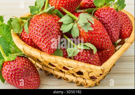 Ein Nahaufnahme reifer, roter Erdbeeren, die aus einem rustikalen Korb überlaufen, garniert mit frischen grünen Blättern. Stockfoto
