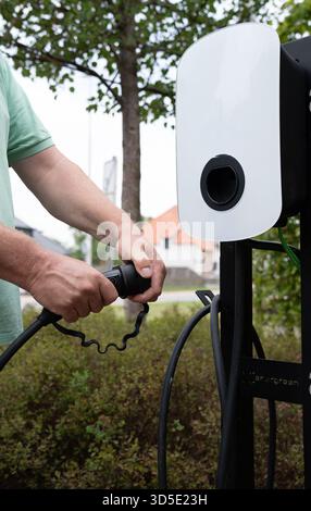 Nahaufnahme der Hände, die Kabel mit einem Ladegerät für Elektrofahrzeuge verbinden Stockfoto