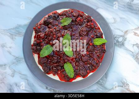 Blick von oben auf cremigen Käsekuchen mit glänzenden gemischten Beeren und Minzblättern. Stockfoto