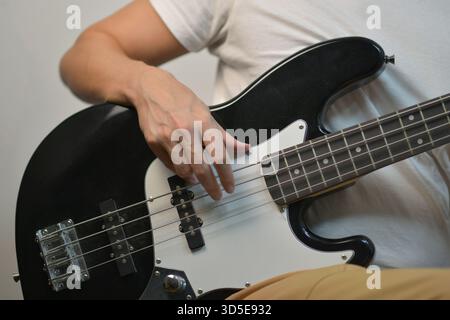 Nahaufnahme eines Mannes, der die Saiten einer schwarzen E-Bass-Gitarre zupft. Konzentrieren Sie sich auf die Handposition, die Instrumentendetails und die musikalische Darbietung. Stockfoto