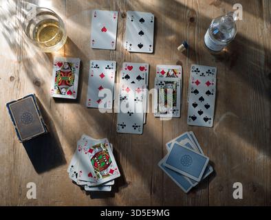 SOLITAIRE GEDULD KARTENSPIEL AUF KIEFERNTISCH MIT TALISKER WHISKEY UND GLAS MIT STARKEN SCHATTEN UND SCHIMMERNDEM LICHT Stockfoto