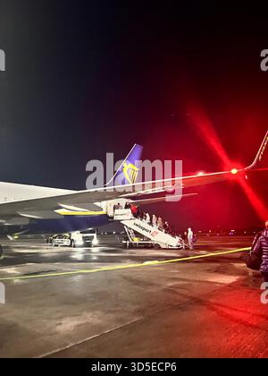 Dramatische nächtliche Szene eines Ryanair-Flugzeugs auf dem Asphalt in Leeds, beleuchtet von intensiven roten Lichtern und umgeben von Reflexionen auf dem nassen Asphalt. Stockfoto