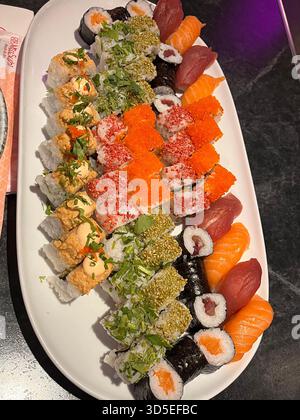 Eine wunderschön angeordnete Sushi-Platte mit lebhaften Brötchen, Sashimi und Beilagen, serviert auf einem weißen Gericht. Gefangen in einem Restaurant in Alicante, Stockfoto
