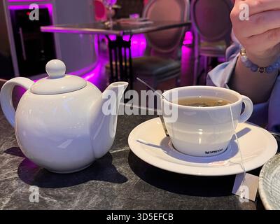 Ein warmes und einladendes Café in Alicante mit weißer Teekanne, Teetasse und Untertasse auf einem dunklen Tisch. Stockfoto