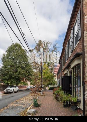 Eine von Bäumen gesäumte Kopfsteinpflasterstraße mit historischen roten Backsteingebäuden, dunklen Fensterläden und einer amerikanischen Flagge in der malerischen Stadt New Castle, Delawar Stockfoto