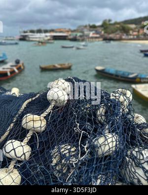 Armação dos Búzios, Rio de Janeiro, Brasilien. Fischernetz mit weißen Schwimmern im Vordergrund, mit Blick auf einen kleinen Hafen an einem bewölkten Tag. Stockfoto