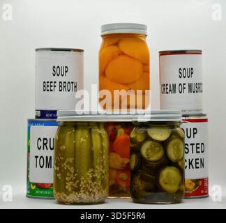 Verschiedene Arten von Suppen aus Dosen und eingelegtem Gemüse sind ordentlich auf einer weißen Oberfläche angeordnet. Diese Kollektion umfasst Rinderbrühe, Pilzcreme und verschiedene eingelegte Artikel. Stockfoto