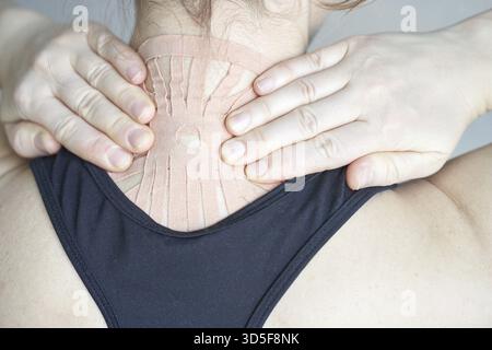 Junge kaukasische Frau, die therapeutisches Klebeband am Hals zur Schmerzlinderung und Muskelunterstützung aufträgt Stockfoto