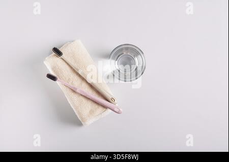 Zwei Zahnbürsten auf einem Handtuch und ein Glas Wasser auf grauem Hintergrund, Draufsicht Stockfoto