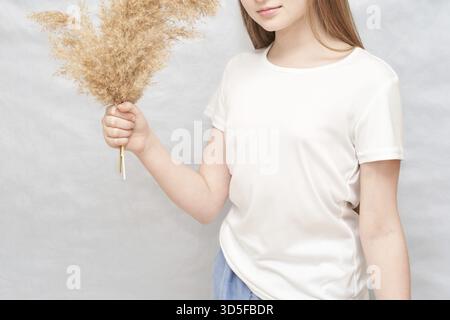 Junge kaukasische Frau mit getrocknetem Pampasgras in lässigem weißem T-Shirt Stockfoto