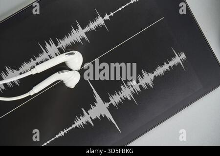 Podcast-Aufzeichnung. Ohrstöpsel und Soundtrack am Tablet. Graues Schwarzweiß. Hörbuch und Podcasting. Audiotechnologie. Hausschulunterricht. Episode bearbeiten Stockfoto