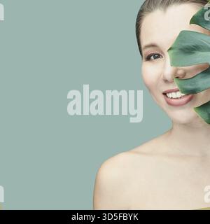 Junge Frau. Lächelnd mit Monstera-Blatt. Modell im Studio. Kosmetologische Gesundheitskonzepte. Wunderschönes tropisches Blatt. Stomatologische medizinische Behandlung. Innengewinde p Stockfoto