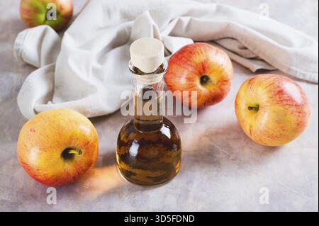 Fermentierter Apfelessig in Glasflasche und Obst auf dem Tisch Stockfoto