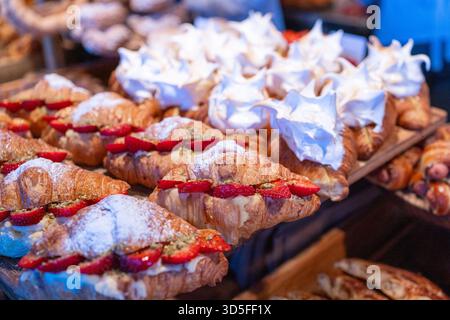 Nahaufnahme von frisch gebackenen Croissants gefüllt mit Sahne und frischen Beeren, mit Puderzucker bestäubt. Leckeres Gebäck für Bäckereimenüs, Food Blogs Stockfoto