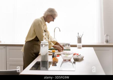 Lächelnde ältere Dame, die hausgemachte Kekse in der modernen Küche zubereitete Stockfoto