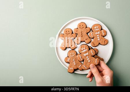 Lebkuchenkekse auf weißem Teller mit Mädchenhand auf grünem Hintergrund. Draufsicht. Stockfoto
