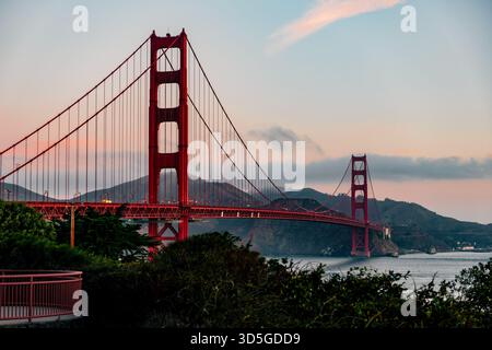 Die legendäre Golden Gate Bridge steht majestätisch vor einem weichen Dämmerhimmel, dessen charakteristischer roter Farbton über der Bucht von San Francisco herausragt. Stockfoto