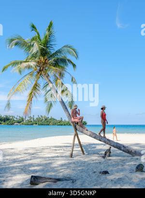 Ein kaukasischer Mann, der auf ein anderes Weibchen achtet, das sich unter der Sonne neben sich wiegenden Palmen und einem lebendigen blauen Meer sonnt. Ein junger Mann, der sich eine andere Frau am Strand in Thailand ansieht, Koh Kood Stockfoto
