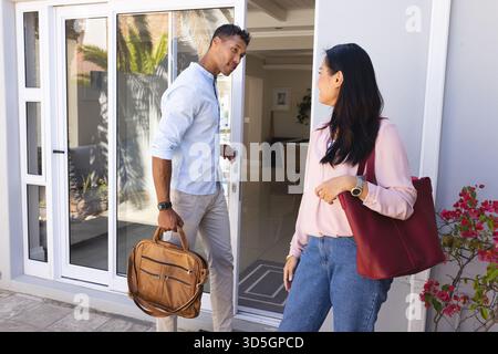 Ein Paar verlässt das Haus, trägt Taschen, lächelt und ist bereit für den neuen Tag Stockfoto