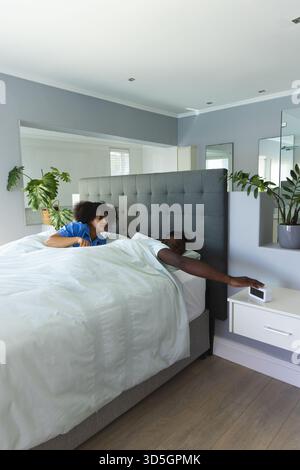 Junges Paar, das in einem modernen Schlafzimmer aufwacht und den Wecker auf dem Nachttisch in der Nähe des Arms ansieht Stockfoto
