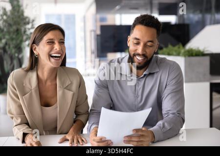 Zwei fröhliche multiethnische Kollegen diskutieren Papierdokumente am Arbeitsplatz Stockfoto