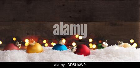 Farbenfrohe Vintage-Weihnachtskugeln im Schnee auf einem hölzernen Hintergrund mit Weihnachtsbeleuchtung, Weihnachtskugeln oder saisonalem Hintergrund Stockfoto