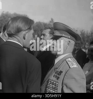 UdSSR, Ukrainische SSR, Slawjansk, 1975. Ein beeindruckendes Nahporträt eines hochrangigen sowjetischen Militärs oder Veteranen beim 30. Siegtag im Lenin Park (Shekowitschy Park). Der hochdekorierte Mann, der eine Paradeuniform und eine Spitzenmütze trägt, ist mit zahlreichen Orden und Orden bedeckt, die seinen Dienst belegen. Er ist im Profil zu sehen, in einem Gespräch mit einem zivilen Gast während der feierlichen Zeremonie. Dieses archivierte Schwarzweiß-Foto bietet einen intimen Blick auf einen Ehrengast an einem großen sowjetischen Feiertag. Stockfoto