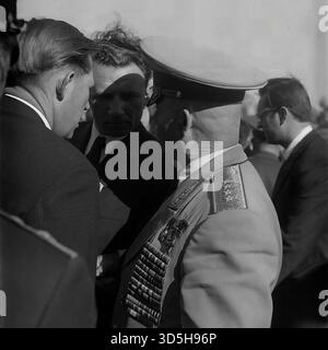 UdSSR, Ukrainische SSR, Slawjansk, 1975. Ein beeindruckendes Nahporträt eines hochrangigen sowjetischen Militärs oder Veteranen beim 30. Siegtag im Lenin Park (Shekowitschy Park). Der hochdekorierte Mann, der eine Paradeuniform und eine Spitzenmütze trägt, ist mit zahlreichen Orden und Orden bedeckt, die seinen Dienst belegen. Er ist im Profil zu sehen, in einem Gespräch mit einem zivilen Gast während der feierlichen Zeremonie. Dieses archivierte Schwarzweiß-Foto bietet einen intimen Blick auf einen Ehrengast an einem großen sowjetischen Feiertag. Stockfoto