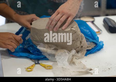 Potters Hände schneiden präzise einen großen Klumpen Ton mit einem Drahtwerkzeug auf einem Tisch Stockfoto