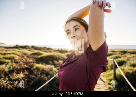 Frau, die die Arme im Freien auf einem Küstenweg ausdehnt und ein Fitnesstraining genießt Stockfoto