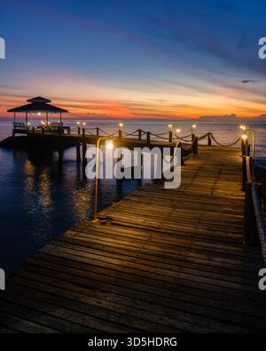 Erleben Sie einen atemberaubenden Sonnenuntergang über dem ruhigen Wasser der Insel Koh Kood, mit einem bezaubernden Holzpier, beleuchtet von sanften Lichtern in Thailand Stockfoto