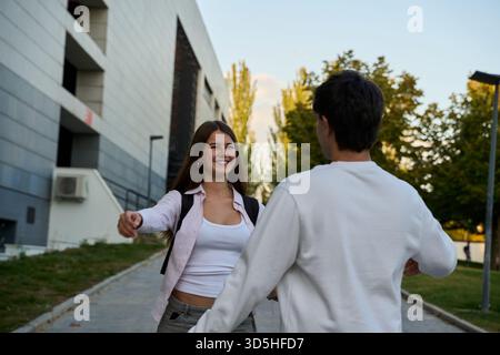 Junge Studenten, die lächeln, umarmen und sich draußen auf einem Universitätscampus wiederfinden, zeigen starke Freundschaft und Liebe Stockfoto