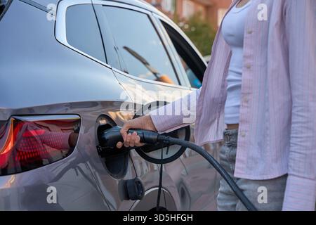 Frauenhand, die das Autoladegerät in ein Elektrofahrzeug einsteckt, symbolisiert nachhaltigen Transport und umweltfreundliche Technologie Stockfoto