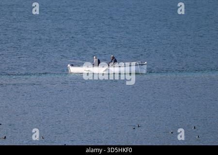 Zwei Leute fischen von einem kleinen weißen Ruderboot aus auf ruhigem blauem Seewasser, aus der Ferne gesehen. Stockfoto
