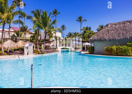 Wunderbarer Blick auf den Pool des Resorts mit hohen Palmen und Leute, die sonniges Wetter in der Nähe des klaren türkisfarbenen Wassers genießen. Punta Cana. Dominikanische Republik. Stockfoto