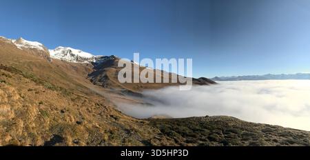 Panorama-Spätherbstlandschaft in den Schweizer Alpen Engadin, mit Morgennebel, der talaufwärts kommt, und sonnendurchfluteten goldenen Berghängen, Schweiz Stockfoto