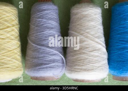 Verschiedene Farben von Alpakawolle und Seide. Kegel aus mehrfarbigem Garn. Wollfäden in einer Reihe. Reihe blauer, weißer, gelber und grauer Wolle. Strickhobbyarbeit. Stockfoto