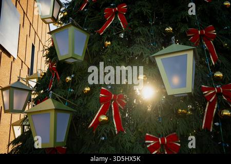 Großer Weihnachtsbaum mit geometrischen Laternen-Dekorationen, Schleifenakzenten und glänzenden Goldkugeln, die über dichte Zweige angeordnet sind, organisieren sich Stockfoto