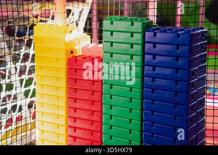 Hohe Stapel von leuchtenden Kunststoffbausteinen in Gelb, Rot, Grün und Blau, die in einer Spielzone für Kinder im Innenbereich mit Sicherheitsnetz und c ausgestellt sind Stockfoto