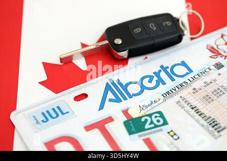 Alberta canadian Autokennzeichen und Zündschlüssel auf der Flagge von Kanada Nahaufnahme. Führerschein- und Zulassungskonzept Stockfoto