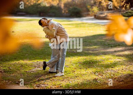 Koreanerin und Kaukasier. Inmitten farbenfroher Herbstlaub umarmt eine Koreanerin einen kaukasischen Mann in einer ruhigen Parklandschaft und genießt einen wunderschönen Tag. Stockfoto