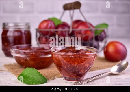Hausgemachte Pflaumenmarmelade in einer Glasschale vor dem Hintergrund frischer Pflaumen. Stockfoto