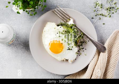 Traditionelles englisches Frühstück mit Spiegeleiern mit Rucola microgreen in grauer Keramikplatte auf grauem Beton altem Hintergrund. Draufsicht. Stockfoto
