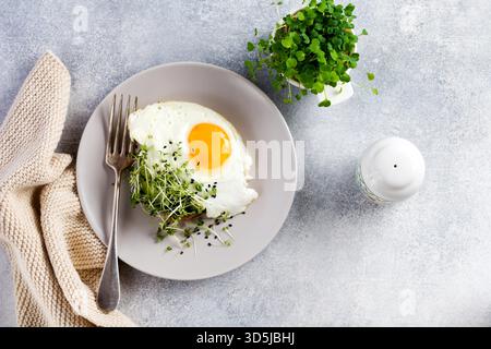 Spiegeleier mit Rucola microgreen in grauer Keramikplatte auf grauem Beton altem Hintergrund. Traditionelles englisches Frühstück. Draufsicht Stockfoto