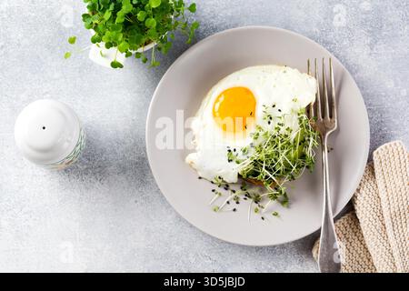 Spiegeleier mit Rucola microgreen in grauer Keramikplatte auf grauem Beton altem Hintergrund. Traditionelles englisches Frühstück. Draufsicht Stockfoto